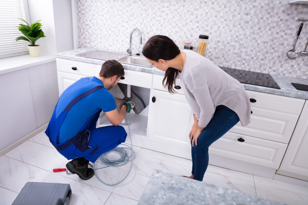 Woman,Looking,At,Male,Plumber,Cleaning,Clogged,Sink,Pipe,With